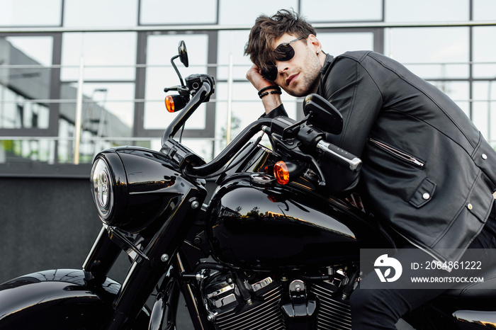 handsome young man in leather jacket resting while sitting on new black motorcycle