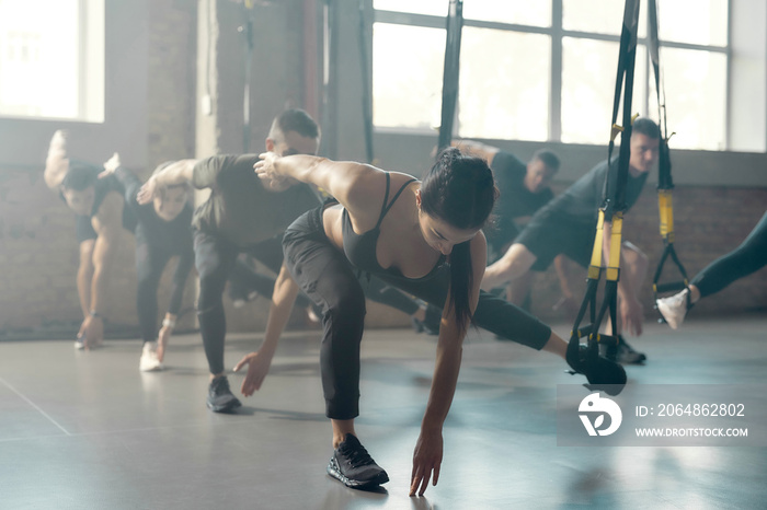 Fitness Center. Portrait of men and women doing fitness training exercises at industrial gym. Straps