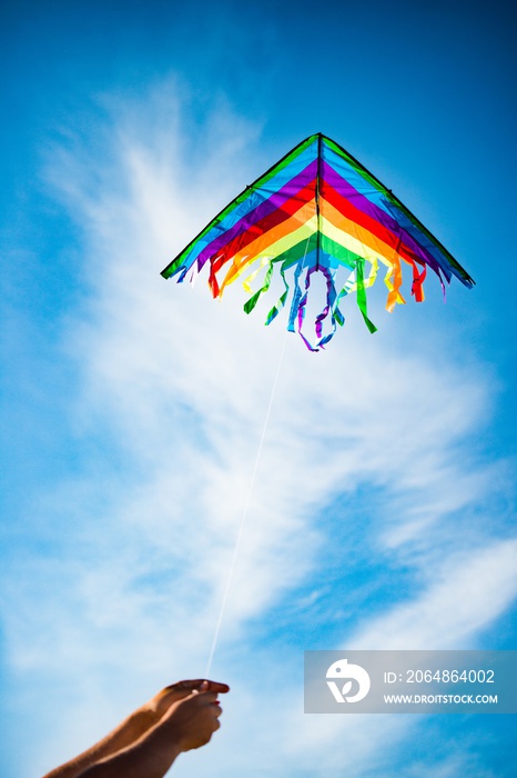 在蓝天白云的背景下，手牵着美丽明亮的彩虹彩色风筝。