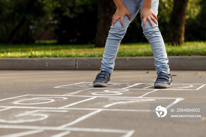 小男孩的腿和在沥青上画的跳房子的特写。孩子在playgro上玩跳房子游戏