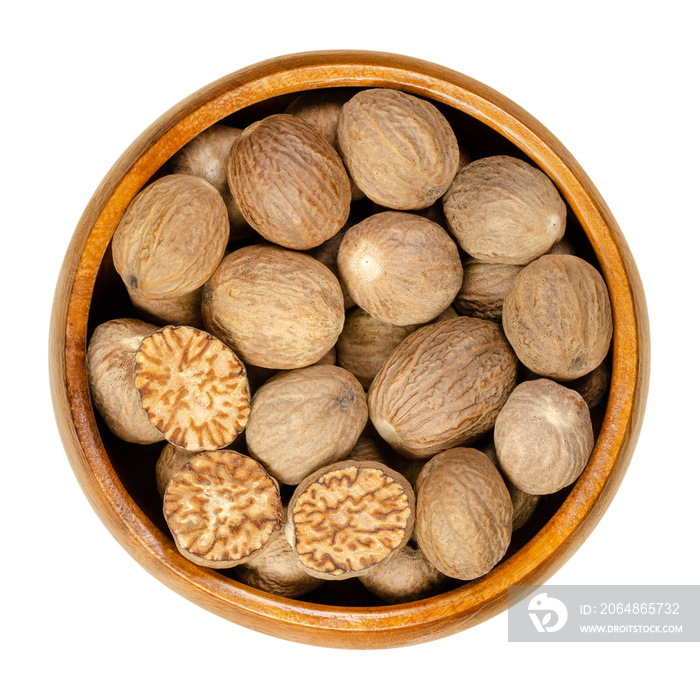 Whole and halved nutmegs in a wooden bowl. Fragrant or true nutmegs, dried seeds of Myristica fragra