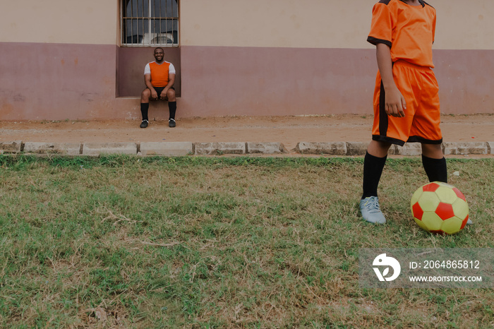 Father sitting and watching son stand with football