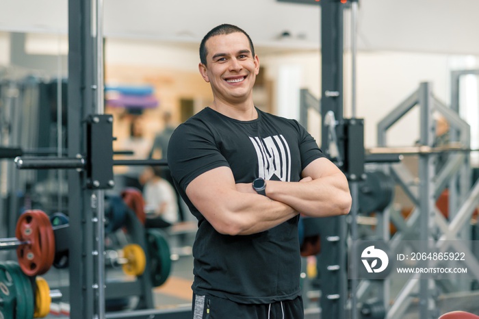 Portrait of muscular sporty smiling man in the gym, handsome professional gym instructor looking at 