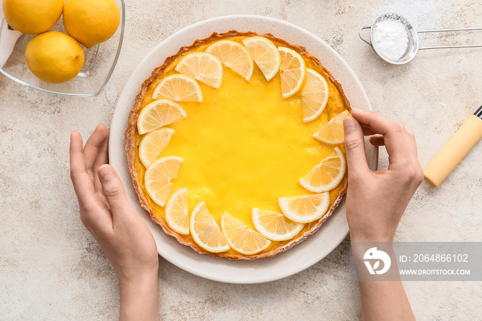 Woman decorating tasty lemon pie on light background