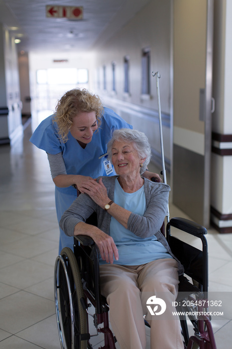 Female nurse comforting senior patient in wheelchair in hospital corridor