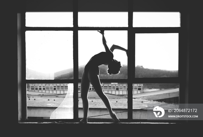 Black and white photo of ballerina in the window frame in an old building.