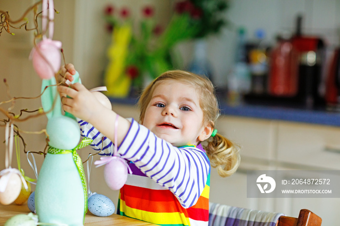 Cute little toddler girl decorating tree and bunny with colored pastel plastic eggs. Happy baby chil