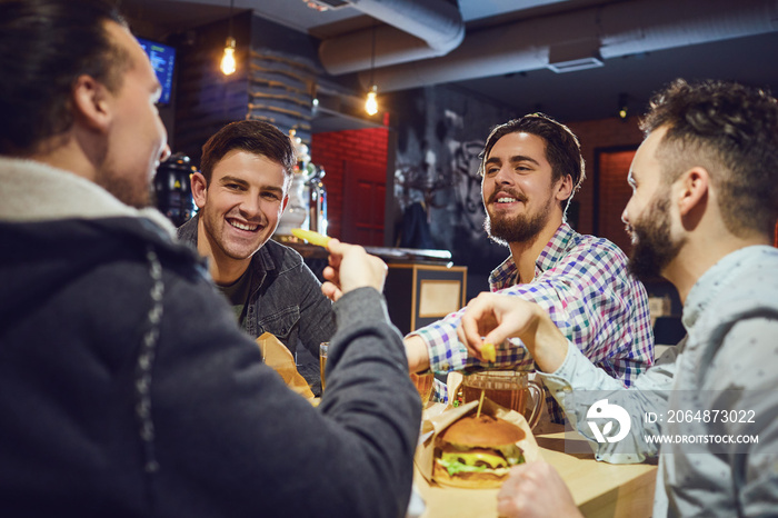 Happy friends eat burgers, drink beer in a bar.