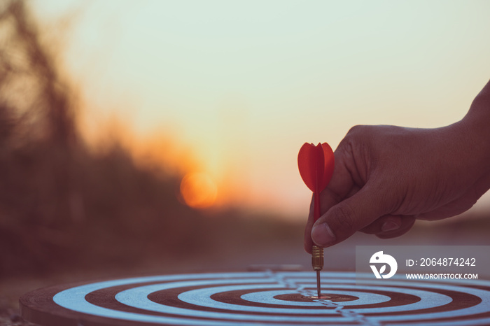 Close up hand hitting red arrow to target dartboard at sunset background. Business targeting and foc