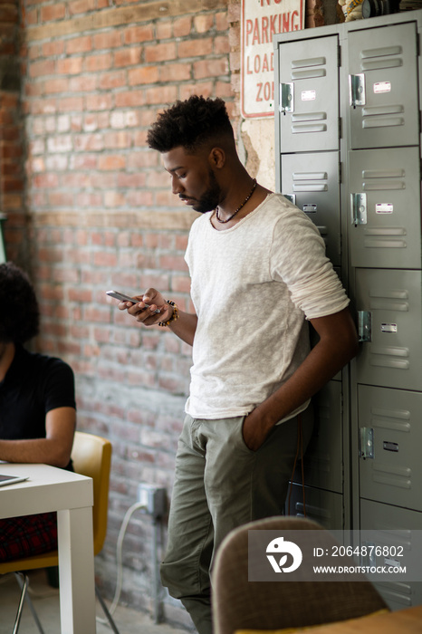 Male executive using smart phone while standing against lockers by coworker at office