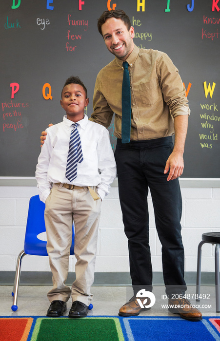 Portrait of teacher and schoolboy (8-9) standing side by side before blackboard smiling