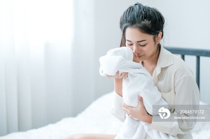 Close up shot of Asian mother kiss her newborn baby in front of white curtain in bedroom.