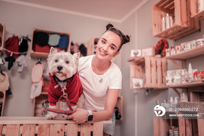 Dark-haired woman smiling after putting red clothing on dog