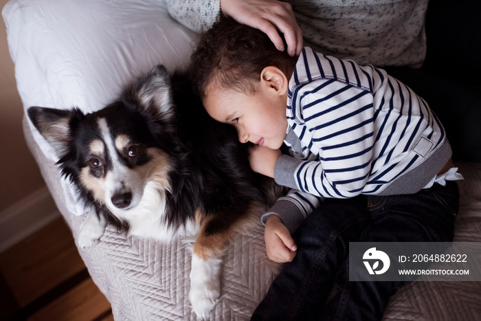 Midsection of mother with cute son and dog relaxing on bed at home