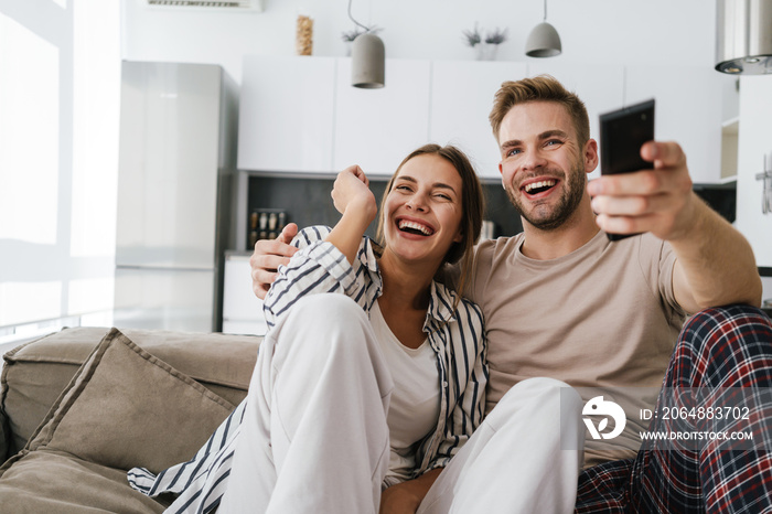 Young couple sitting on sofa and holding remote control at home