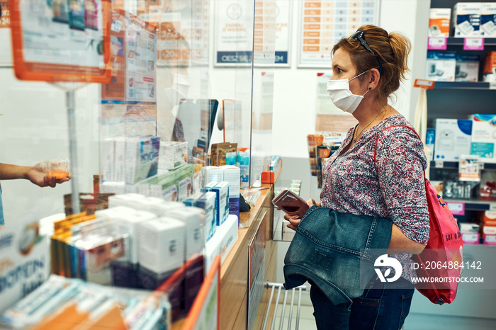 Woman shopping at pharmacy, buying medicines, wearing face mask to cover mouth and nose during pande