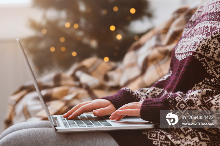 Woman in warm sweater using laptop over Christmas decorating room