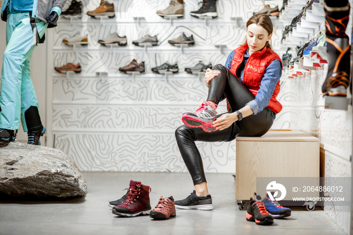 Woman trying shoes for mountain hiking sitting in the fitting room of the modern sports shop