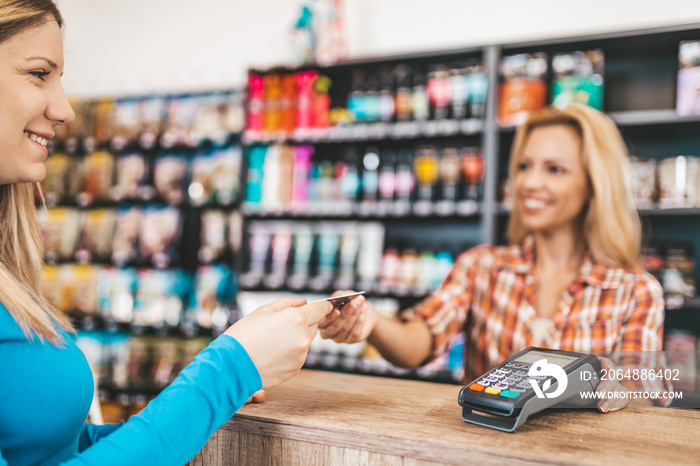 Smiling saleswoman working at pet shop checkout. Electronic payment with card.