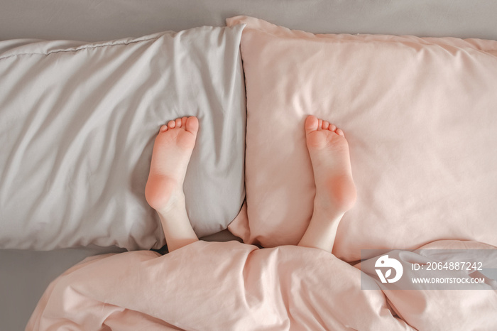 Kids child legs feet lying on pillows in bed at home. Child playing hide and seek game under blanket