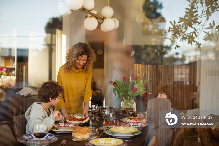 Mother serving pizza to boys on dining table at home seen through window