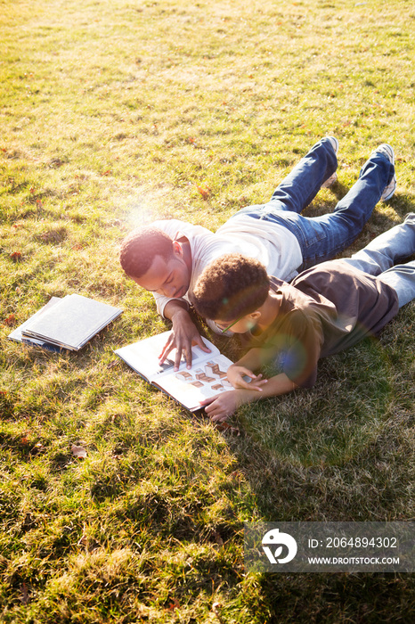 Father and son lying on lawn reading book