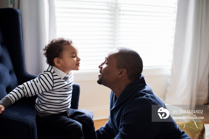 Side view of smiling father looking at cute son sitting on armchair against window in room