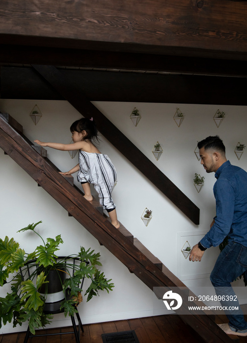 Side view of father and daughter climbing on steps at home