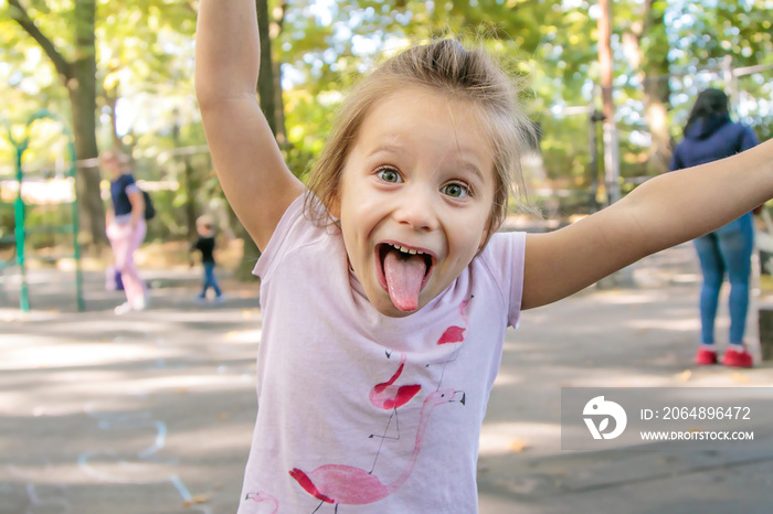 Happy four year old girl making a silly face with a stuck out tounge while playing on a playground.