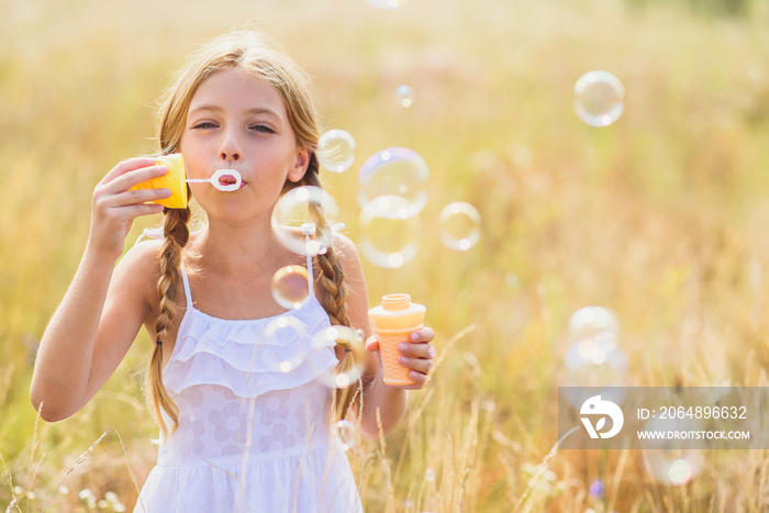 Cute child blowing soap bubbles in meadow