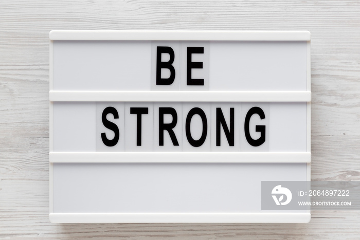 Be strong words on a lightbox on a white wooden surface, top view. Overhead, from above, flat lay.