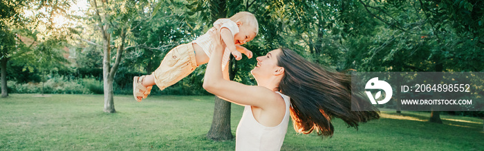 Young mother spinning toddler baby boy outdoors. Parent playing with child son in park. Authentic li