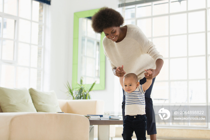 Mother helping cute baby son learn to walk in living room