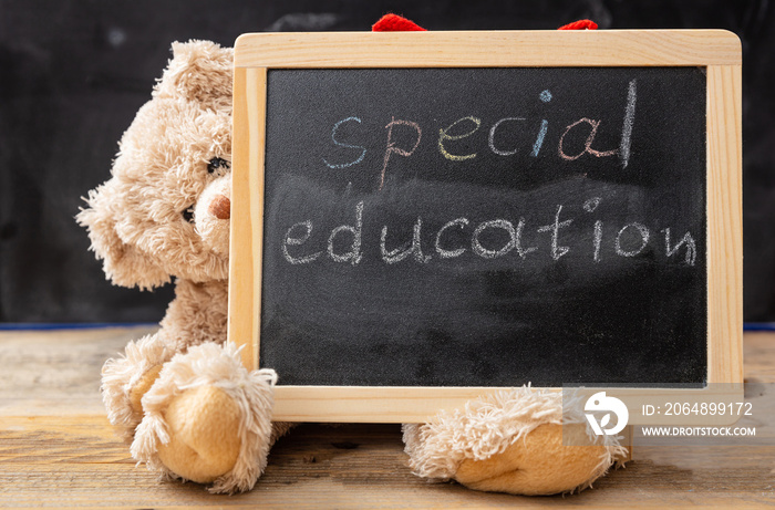 Teddy bear hiding behind a blackboard. Special education text drawing on the blackboard