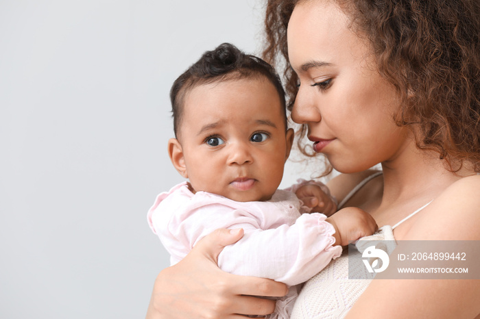 African-American woman with cute little baby on light background