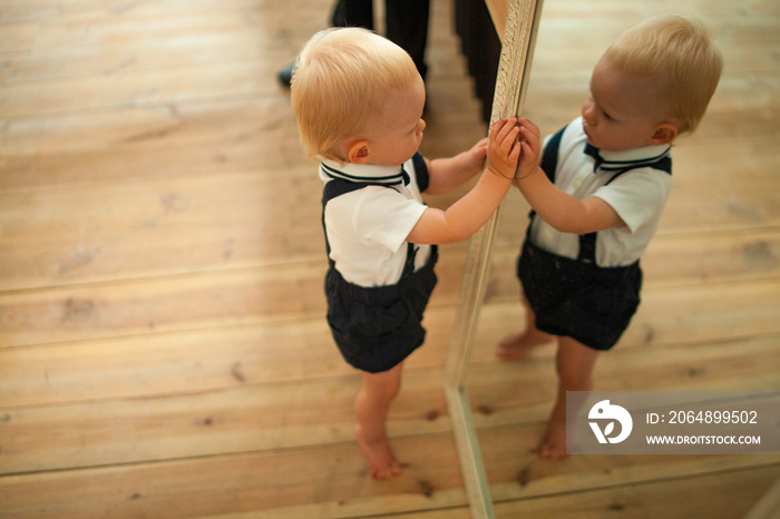 Baby boy plays near the mirror with his reflection.