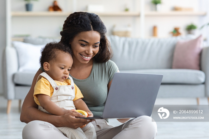 现代技术。带着婴儿的年轻黑人妇女在家使用笔记本电脑