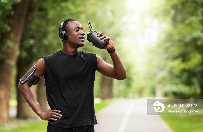 Athletic black man drinking protein while training at park