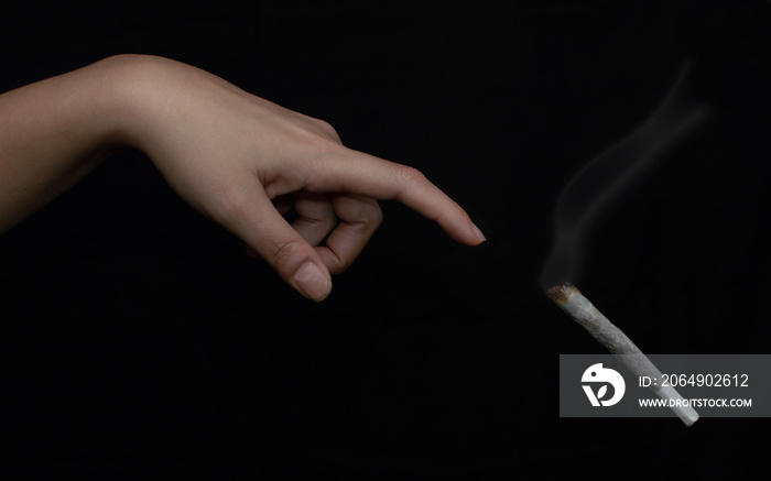 Artistic cannabis background: Hand about to touch a big lit joint of marihuana or cigarette isolated