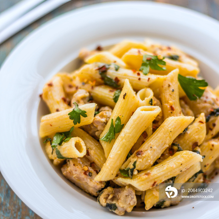 Alfredo Penne Pasta With Chicken and Herbs Served In a Bowl, Closeup Square Image.