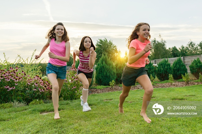 三个年轻的运动女孩，十几岁的青少年，在夏日日落的背景下，在绿色的草坪上奔跑。