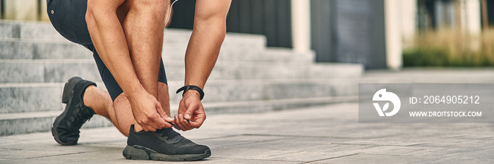 A man  in a light athletic uniform ties a lace on a shoe for  running. Sport concept