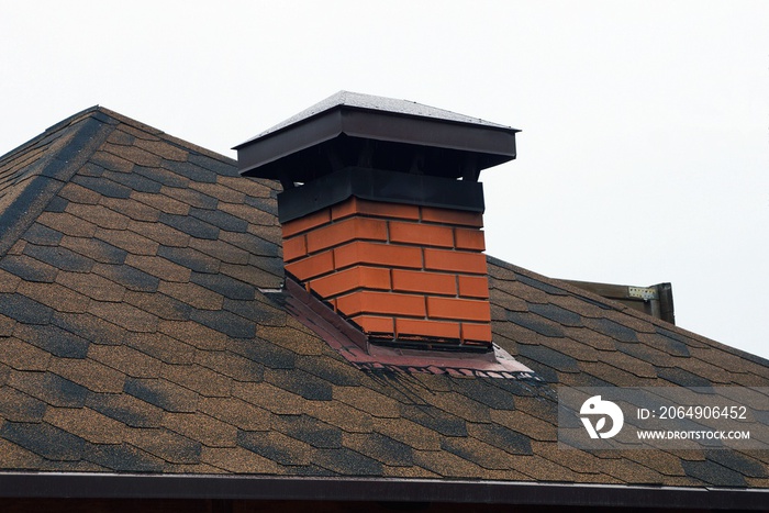 brick chimney on the brown tiled roof of a private house against the sky