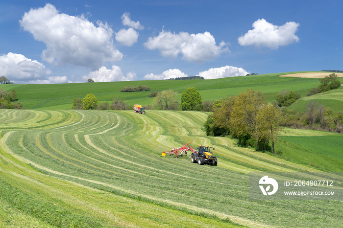 Zwei Traktoren bei der Ernte von Grünfutter in hügeliger Landschaft