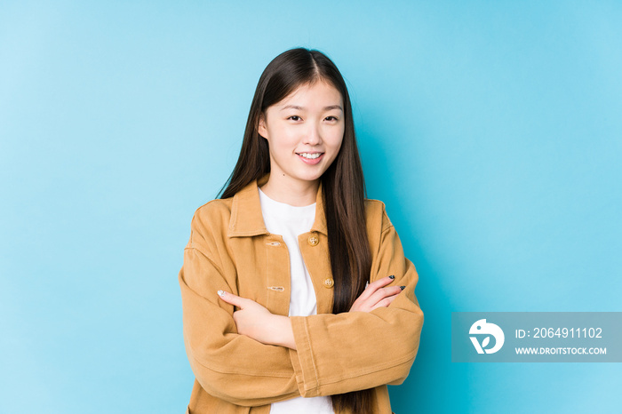 Young chinese woman posing in a blue background isolated who feels confident, crossing arms with det