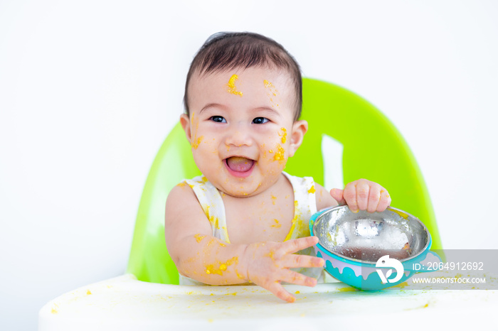 Cute baby happy to eat and play baby food mashed rice mixed with crushed pumpkin in high chair.