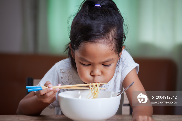 Cute asian child girl eating delicious instant noodles with chopsticks for her lunch in the house