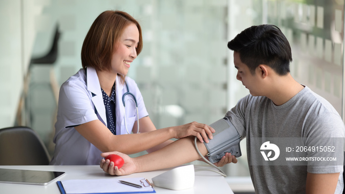 Young Asian female doctor checking blood pressure of male Asian patient