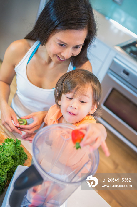 男性幼儿和母亲将草莓放入厨房柜台上的搅拌机的高角度视图