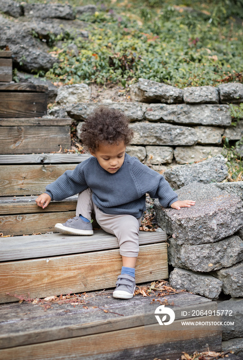 Biracial toddler walking down outdoor steps in backyard garden during fall